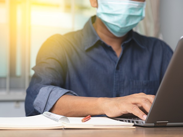 Man wearing mask working on laptop